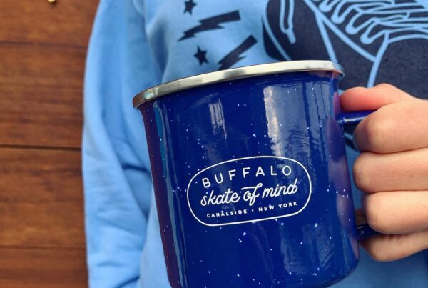 closeup of person holding a camp-style mug that reads "Buffalo skate of mind"