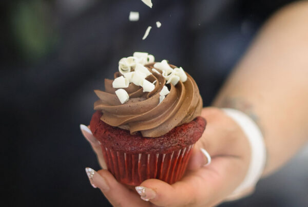 A closeup image of Jasmine Hidalgo holding a red velvet cupcake with chocolate frosting
