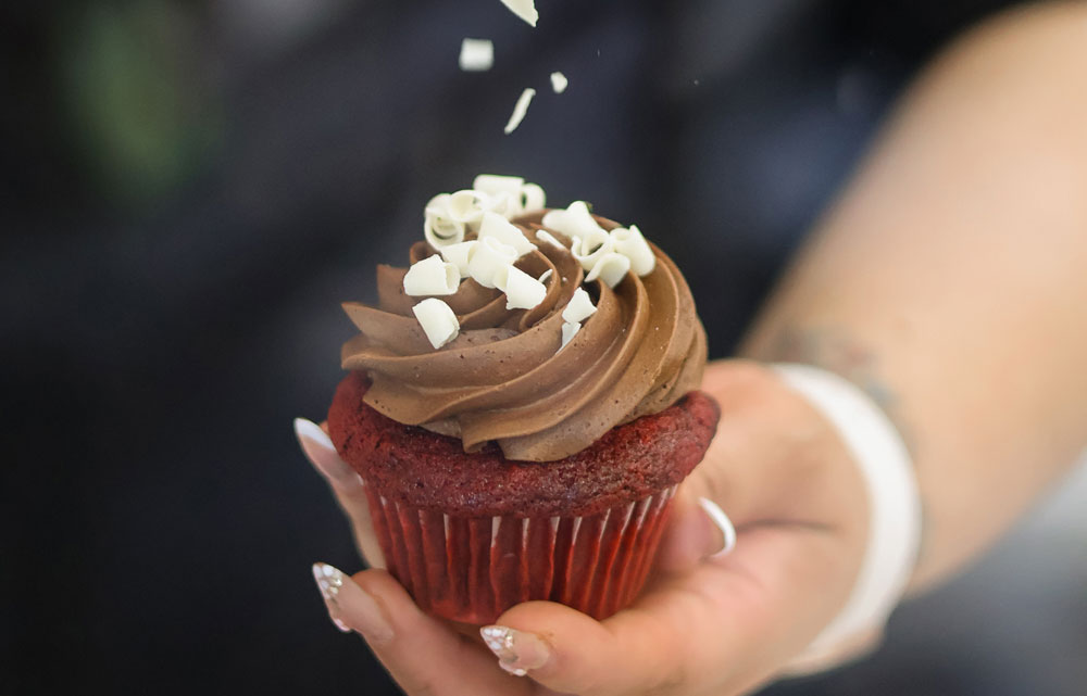 A closeup image of Jasmine Hidalgo holding a red velvet cupcake with chocolate frosting