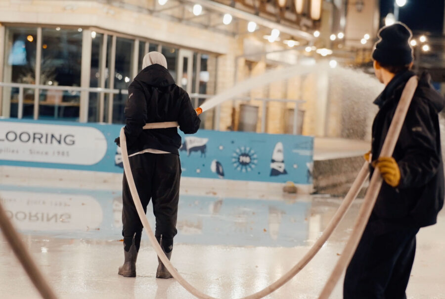 Two people use a fire hose to spray water on the Ice at Canalside
